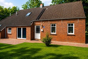A brick house with a tiled roof, a front door, and a small garden.
