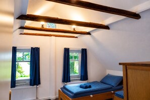 A room with a sloped ceiling, two windows with curtains, a bed with a patterned bedspread, and a radiator.