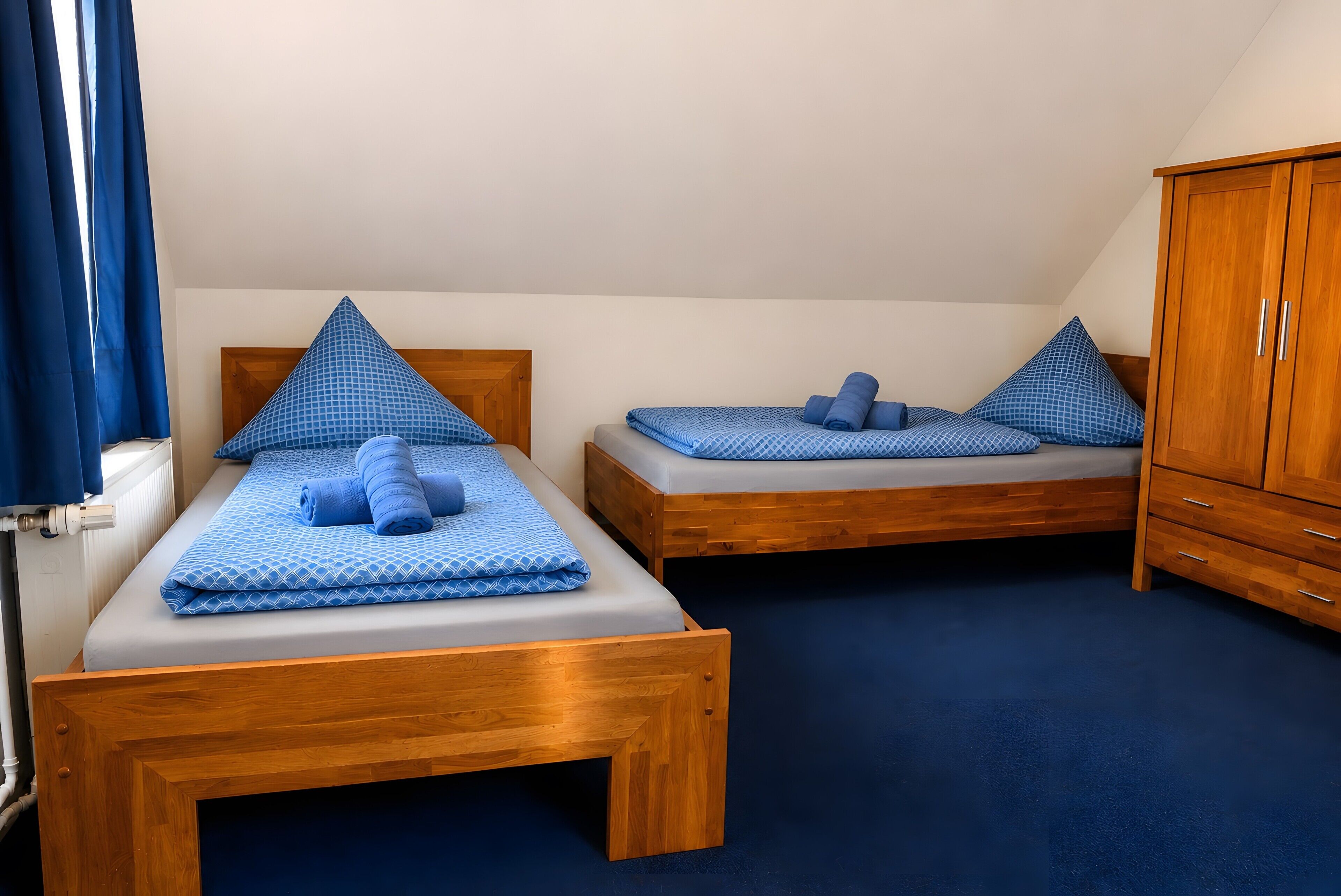 A room with two wooden beds, a wardrobe, and a blue carpet.