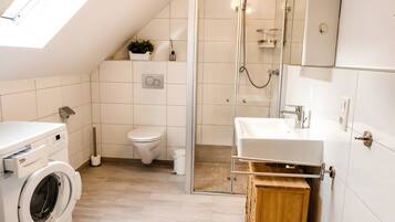Ein modernes Badezimmer mit Waschmaschine, Toilette, Dusche und Waschbecken.