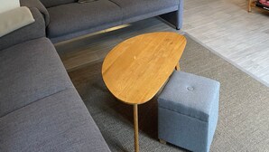 A living room with a grey sofa, a wooden coffee table, and a dining area with a table and chairs. - Holiday Home 'Birken' with Shared Garden and Wi-Fi (Hage)