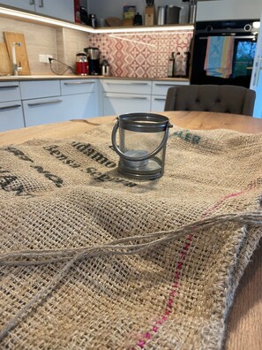 A kitchen with a table covered by a burlap cloth, a metal lantern, and a patterned backsplash.