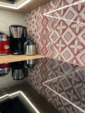 A kitchen with a coffee maker, kettle, and toaster on a wooden shelf.