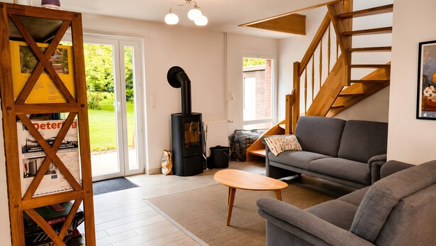 A living room with a sofa, a coffee table, a wooden bookshelf, a fireplace, and a staircase. - Holiday Home 'Birken' with Shared Garden and Wi-Fi (Hage)