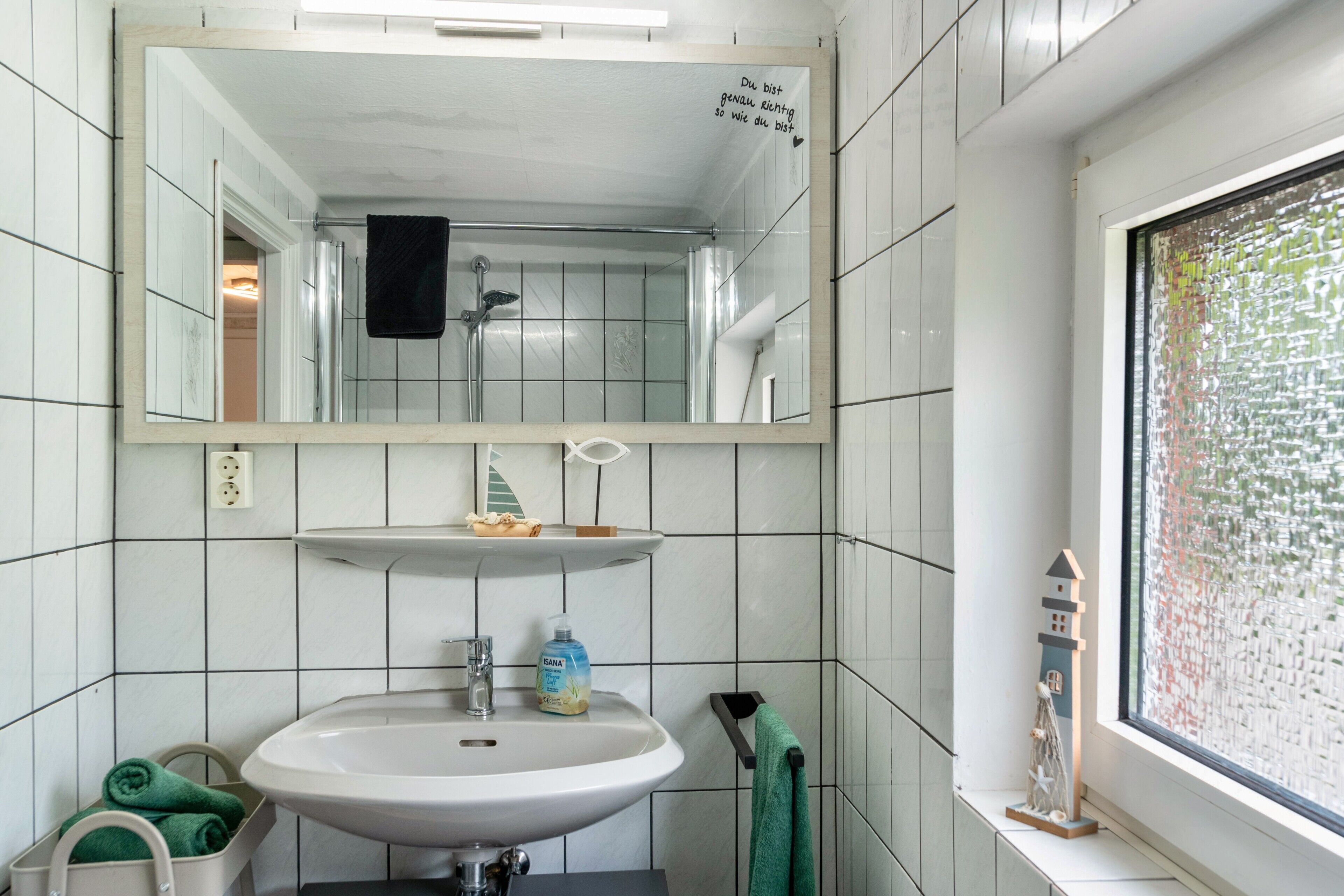 A bathroom with a white sink, mirror, and tiled walls.