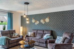 A living room with a grey patterned wall, a brown sofa set, a coffee table, and pendant lighting.