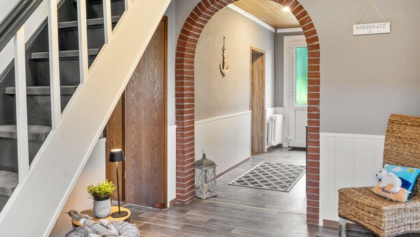 A staircase with a wooden finish, a brick archway, a wicker chair with a cushion, and a hanging sign. - Holiday Home 'Jollenhuus' with Private Terrace, Private Garden and Wi-Fi (Ihlow)