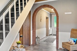 A staircase with a wooden finish, a brick archway, a wicker chair with a cushion, and a hanging sign. - Holiday Home 'Jollenhuus' with Private Terrace, Private Garden and Wi-Fi (Ihlow)