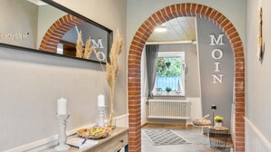 A hallway with a brick archway, a mirror, a white candle, a basket, and a radiator. - Holiday Home 'Jollenhuus' with Private Terrace, Private Garden and Wi-Fi (Ihlow)