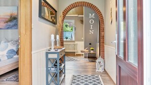 A hallway with a wooden floor, a bed with patterned pillows, a table with candles, and a large archway with the word 'MOIN' on it. - Holiday Home 'Jollenhuus' with Private Terrace, Private Garden and Wi-Fi (Ihlow)