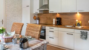 A kitchen with white cabinets, a wooden countertop, a built-in oven, and wicker chairs. - Holiday Home 'Jollenhuus' with Private Terrace, Private Garden and Wi-Fi (Ihlow)