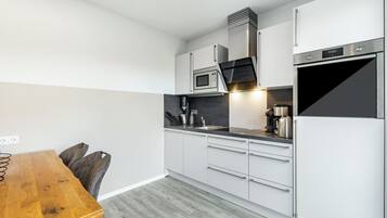 A modern kitchen with white cabinets, stainless steel appliances, a wooden dining table, and a black countertop.