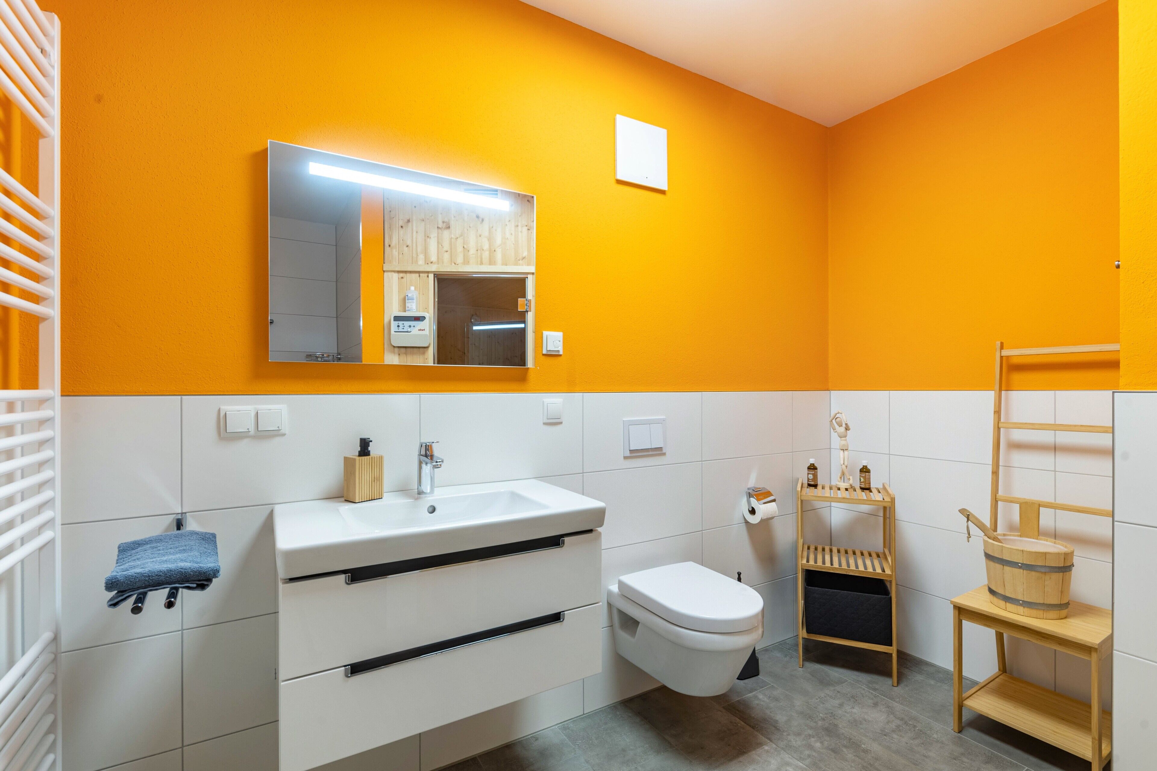 Ein Badezimmer mit einem weißen Waschbecken, einer Toilette, einem Spiegel und einem Holzregal mit Toilettenartikeln.