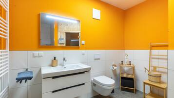 Ein Badezimmer mit einem weißen Waschbecken, einer Toilette, einem Spiegel und einem Holzregal mit Toilettenartikeln.