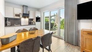 A modern kitchen with a dining area, a flat-screen TV, and a sliding glass door to a patio. - Holiday Home 'Diemelblick' with Lake View, Private Terrace and Wi-Fi (Diemelsee)
