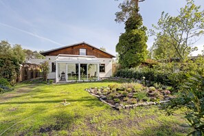 Una casa con un invernadero, un jardín bien cuidado y fachada de madera.