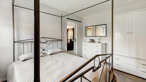 Une chambre à coucher comprenant un lit à baldaquin avec une tête de lit, une table de chevet, une commode et une armoire.