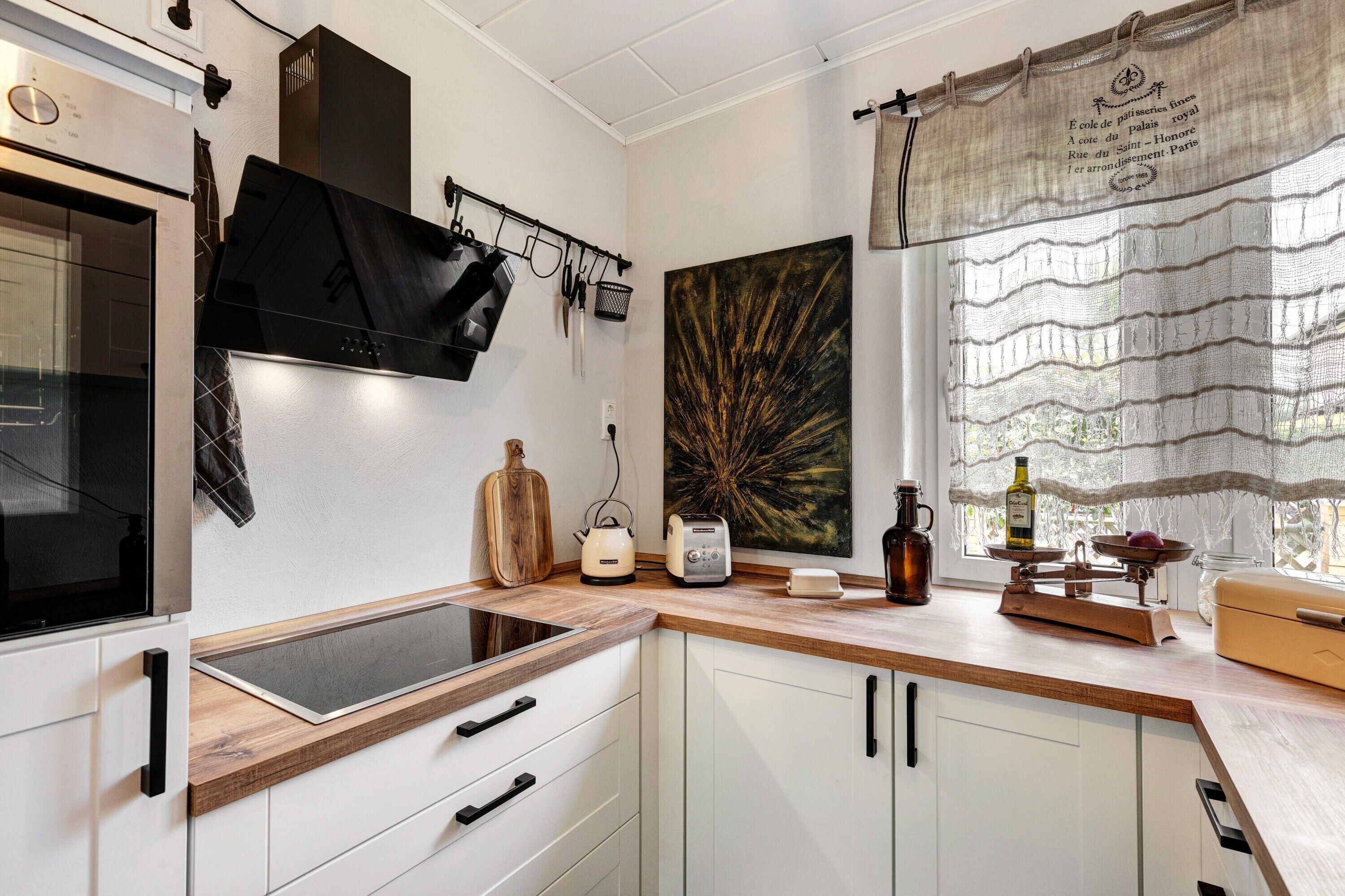 Una cocina moderna con armarios blancos, encimera de madera, horno empotrado y diversos electrodomésticos.