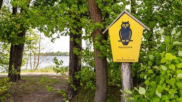 A sign for Naturpark Land Brandenburg with an owl symbol, surrounded by trees and a lake view.