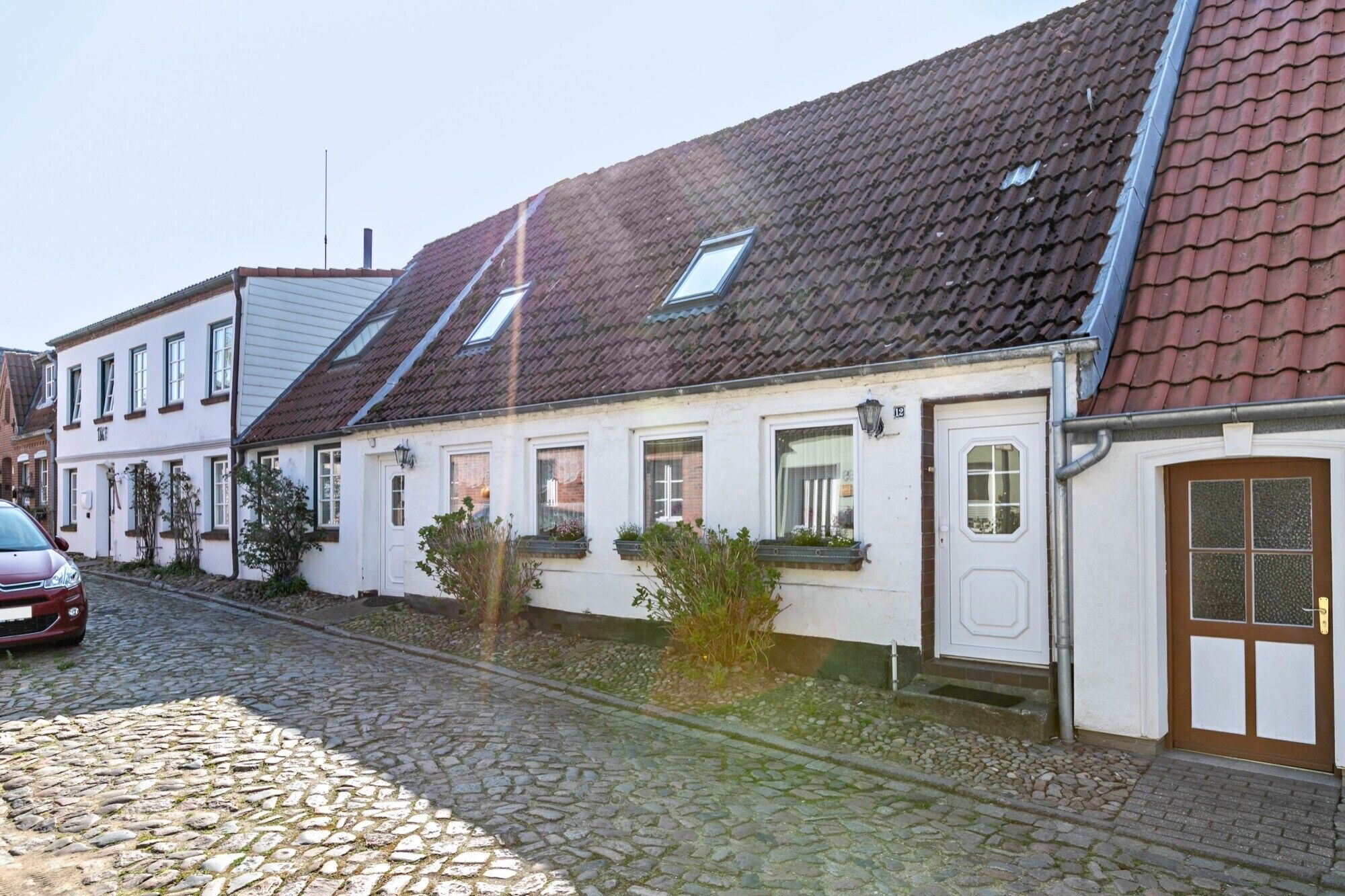 A row of traditional European-style houses with sloped roofs, a cobblestone street, and a parked car.