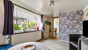 Een kamer met een raam, radiator, tafel met decoratief bord, een stoel, een televisie en een wand met een patroon.