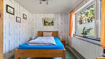 Ein Schlafzimmer mit einem hölzernen Bett, einem Fenster mit Vorhängen, einer Heizung und gerahmten Bildern an der Wand.