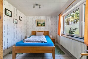 Une chambre à coucher avec un lit en bois, une fenêtre avec des rideaux, un radiateur et des tableaux encadrés accrochés au mur.