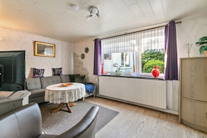 Un salon avec un canapé, une table ronde, un radiateur et une fenêtre avec des rideaux.