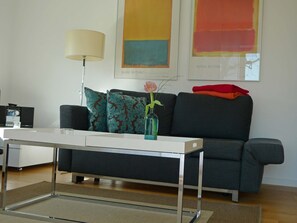 Una sala de estar moderna con un sofá, una mesa de centro, una lámpara y obras de arte en la pared.