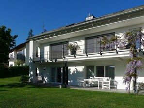 A modern two-story house with a balcony, large windows, and a lawn.