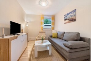 Un salon moderne avec un téléviseur à écran plat, un canapé, une table basse et une fenêtre avec des rideaux.