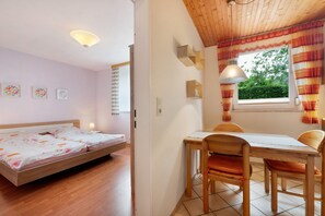 Une pièce comprenant un lit, une table avec des chaises, une fenêtre avec des rideaux et des étagères fixées au mur.