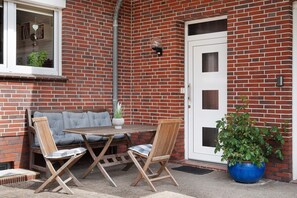 Une façade en briques avec une porte blanche, une petite table avec des chaises et une plante en pot.