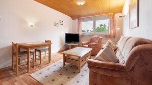 Ett vardagsrum med ett träpanelat tak, en tv, en soffa och ett matbord.