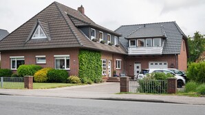 Ett tvåvåningshus med ett sluttande tak, en fasad av tegel och en liten veranda framför huset.