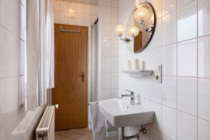 A bathroom with a white sink, a mirror with lights, a towel rack, and a wooden door. - Apartment 'Monika' with Balcony (Butjadingen)