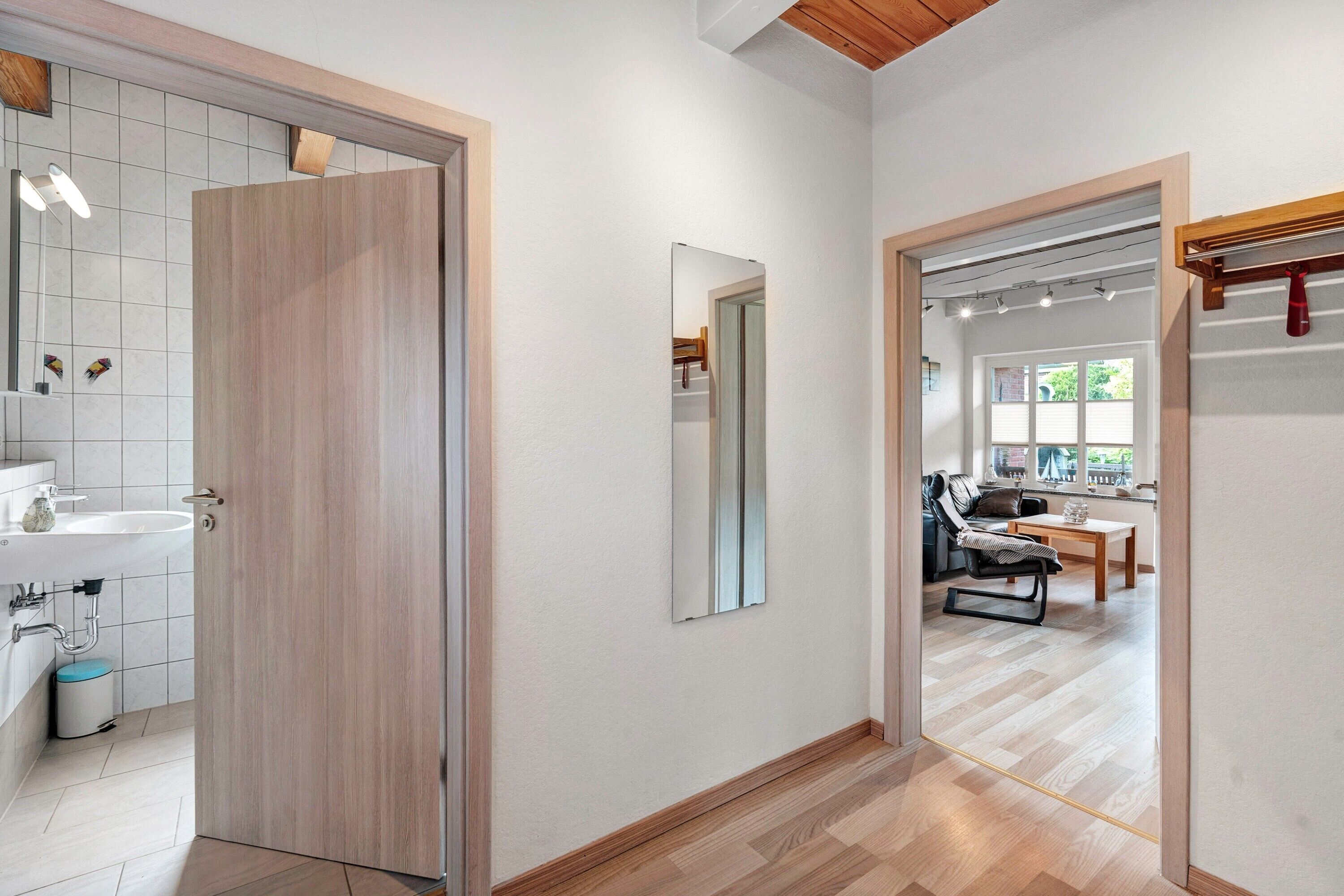 A modern interior with a wooden door, a mirror, a sink, and a dining area with a chair and table.