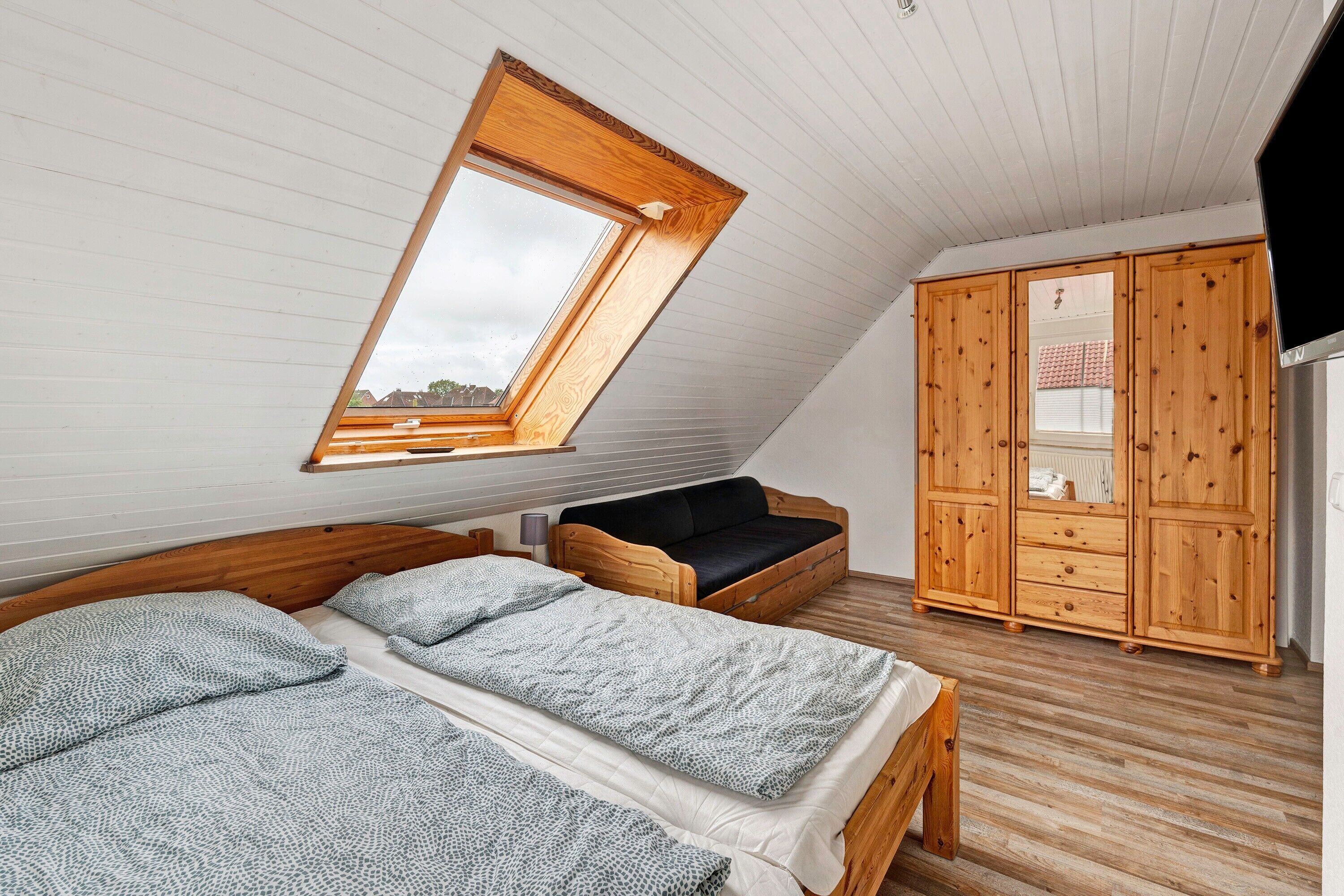 Una camera da letto con soffitto spiovente, una finestra a lucernario, un armadio in legno e un letto con biancheria decorata.