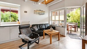 A modern living room with a leather sofa, wooden coffee table, and a view of the garden through large windows. - Holiday Home Little Lighthouse-Backbord Terrace, Garden, Wi-Fi, Bike Garage, EV Charging (Fehmarn)
