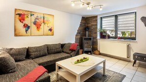 Een woonkamer met een bank, een salontafel, een wereldkaart schilderij, een open haard en een raam met jaloezieën.