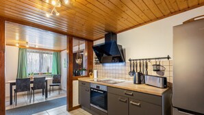Een moderne keuken met een houten plafond, een inbouwoven, een koelkast en een eethoek met een tafel en stoelen.