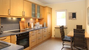 A kitchen with wooden cabinets, a stove, a sink, and a dining area with chairs. - Apartment 'Blum' with Private Terrace, Garden, and Wi-Fi (Schmallenberg)