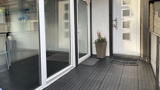 A modern building entrance with glass doors, a welcome mat, and a potted plant. - Apartment 'Blum' with Private Terrace, Garden, and Wi-Fi (Schmallenberg)