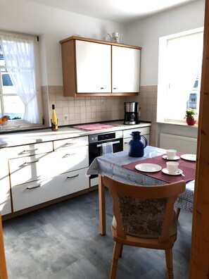 A kitchen with a dining table set for two, a coffee maker, and a bottle on the counter.