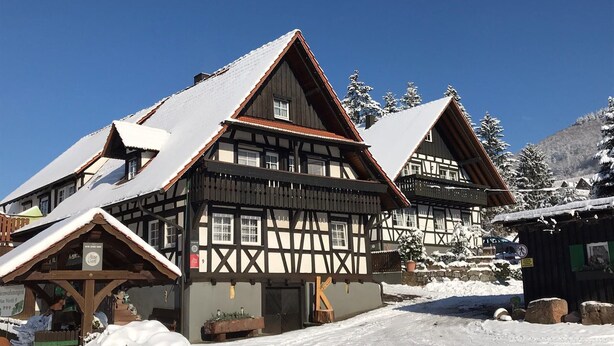A traditional half-timbered building with a snow-covered roof, a wooden fence, and a clear blue sky. - Klaus and Erika Köninger: 'Erika' Apartment with Private Terrace and Wi-Fi (Sasbachwalden)