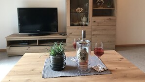 A living room with a TV, wooden cabinet, potted plant, bottle of alcohol, and wine glass on a table. - Klaus and Erika Köninger: Apartment 'Klaus' with Shared Garden and Wi-Fi (Sasbachwalden)