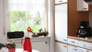 A kitchen with a window, a radiator, a coffee maker, and a table with a red kettle. - Klaus and Erika Köninger: Apartment 'Klaus' with Shared Garden and Wi-Fi (Sasbachwalden)