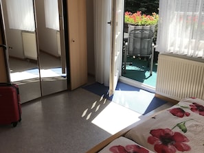 A room with a sliding glass door leading to an outdoor area, a red suitcase, a bed with a floral bedspread, and a radiator.