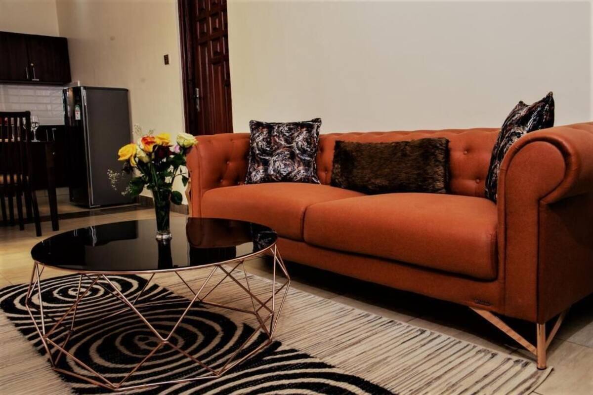 A living room with an orange sofa, black coffee table, and patterned cushions.