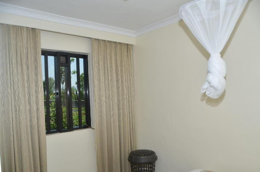 Una habitación con ventana, cortinas, mosquitero y cubo de basura.